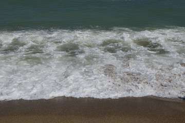 A sea wave flowing the sandy beach with seething foam.