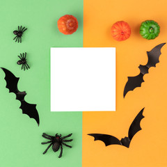 Creative Halloween composition. Pumpkins, bats, spiders and paper blank on orange and green background. Flat lay, top view, copy space