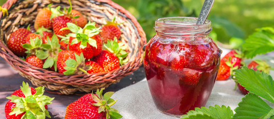 Strawberry jam and juicy ripe strawberries on a wooden table in the garden on a summer sunny...