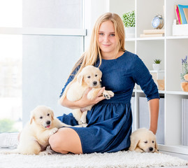 Girl sits on floor with retriever puppies