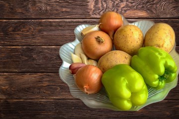 fresh vegetables, onions, garlic, potatoes and green paprika in a plate on a wooden background