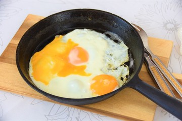 fried eggs in a cast iron pan on a wooden board with a fork and knife