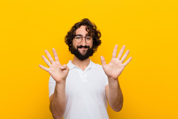 young crazy man smiling and looking friendly, showing number nine or ninth with hand forward,...