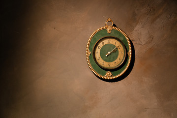 Gold vintage clock with arabic numbers. Beautiful green frame clock hanging on the brown wall. Antique round wall timepiece. Copyspace