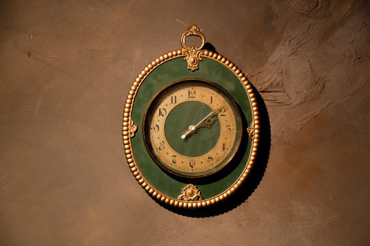 Gold vintage clock with arabic numbers. Beautiful green frame clock hanging on the brown wall. Antique round wall timepiece. Copyspace