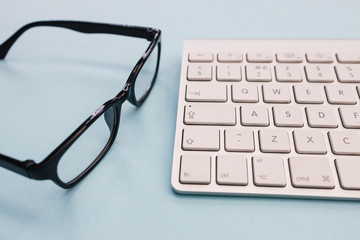 Computer keyboard glasses minimal home office bright blue color background top view