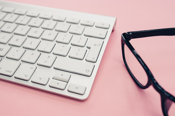 Computer keyboard glasses minimal home office bright pink color background top view