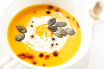 Pumpkin soup close-up in out of focus. Background image.Seasonal food.Soup decorated with cream sauce and pumpkin seeds. White background .Autumn.