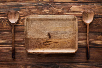 top view of empty rectangular dish between spoons on brown wooden surface with copy space