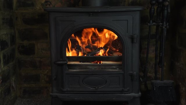 4K Loaded wood burning stove with logs in, lit fire heating British home with flames
