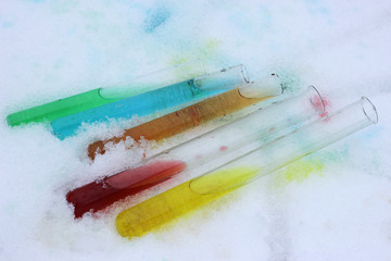Test tubes with aqueous solutions of food dyes lie on the snow.