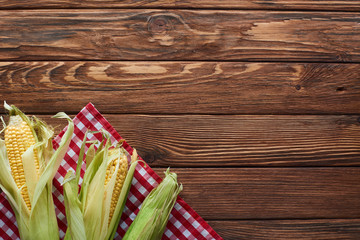 top view of raw corn on checkered tablecloth on wooden surface