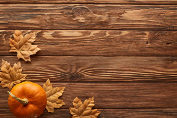 top view of small pumpkin on brown wooden surface with dried autumn leaves
