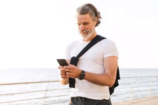 Image of happy old man using earpod and cellphone while working out