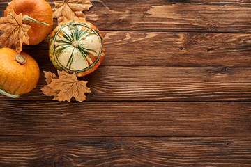 Fototapeta premium top view of fresh pumpkins on brown wooden surface with dry leaves