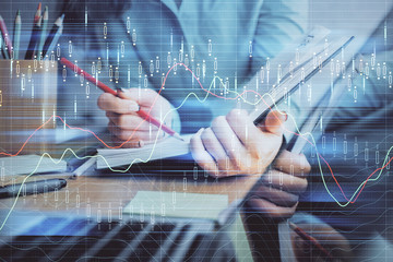 A woman hands writing information about stock market in notepad. Forex chart holograms in front. Concept of research. Multi exposure