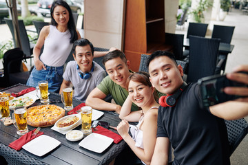 Asian young man making selfie portrait together with his friends on mobile phone during their meeting at the restaurant