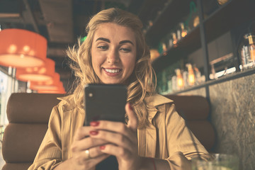 Young charming woman calling with cell telephone while sitting alone in coffee shop during free time, attractive female with cute smile having talking conversation with mobile phone