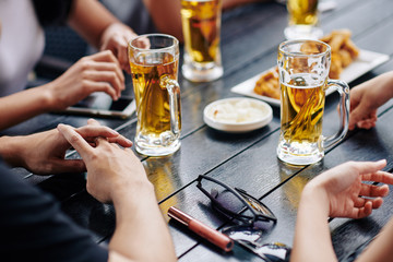 Close-up of young people sitting at the table and drinking beer from the glasses in the bar