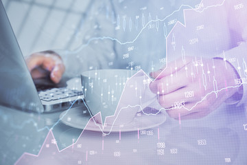 Double exposure of graph with man typing on computer in office on background. Concept of hard work.