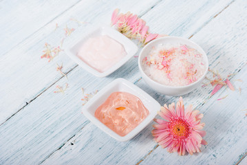Obraz na płótnie Canvas beauty product samples, cosmetic cream, bath salt, liquid soap and pink flower, white wood table