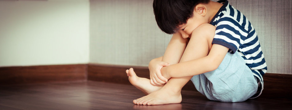 A difficult little Asian boy sits and left alone in room, hugs knees up and face down staring at his toe. Childhood mental health, Unsociable, Introvert kids, Autism, Emotional abuse effects. Banner.