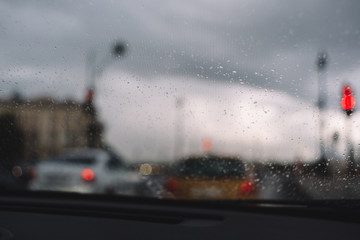 Close up photo of rain drops on windshield. Selective focus, blurred cars in traffic jam on background. Thin threads of glass heating. Rainy season. Automotive industry. Cosiness inside the car.