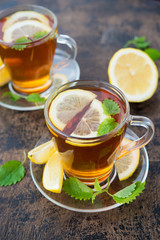 A Cup of hot black tea with mint and lemon stands on a wooden table. Vertical orientation.