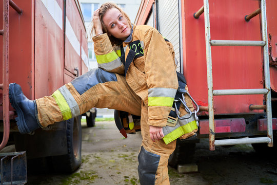 Image of firefighter girl looking at camera next to fire engines on street.