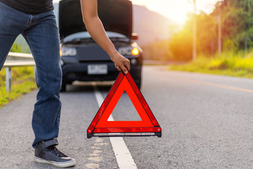 Man hold and put down the red triangle for warning have black color car parking  on road and oper...