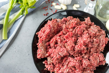 plate of raw minced pork meat with garlic, spices, celery, towel on grey background,