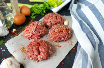 4 meat burgers, pork round cutlets with spices on a black background, towel, eggs, garlic,