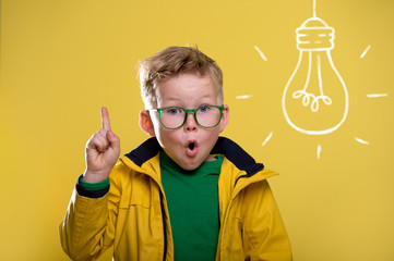 Back to school. Blond child in yellow raincoat and green glasses with light bulb. Funny child with...