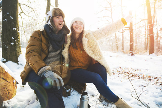 Mann und Frau sitzen im winterlichen wald trinken tee und geniesen die sonnenstunden