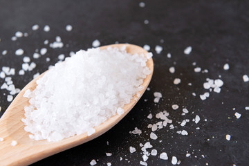 Fototapeta na wymiar salt in a spoon and scattered on the black powdered, coarse salt closeup