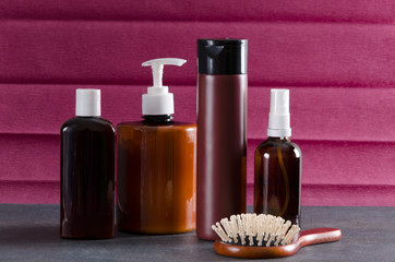 Hair care products on the grey surface against purple background.Brown bottles of hair oil, balm, different types of shampoo and brush