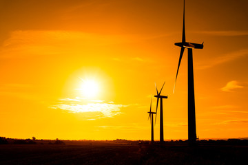 Three wind turbines at sunrise in the English countryside bathed in orange © Studio-FI