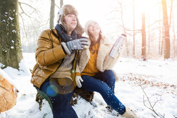 Obraz premium Mann und Frau sitzen im winterlichen wald trinken tee und geniesen die sonnenstunden