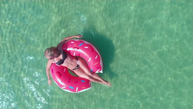 Sexy young girl in sunglasses girl on the pink rubber donut ring posing on the sea with waves