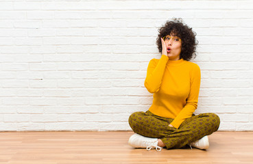young pretty afro woman feeling shocked and astonished holding face to hand in disbelief with mouth...