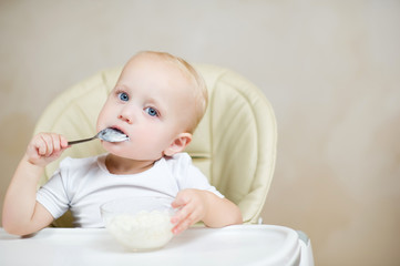 little girl licks a spoon with porridge and looks seriously at the camera