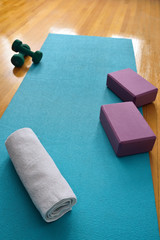 Blue yoga mat in gym studio with oak floor and towel barbells and blocks