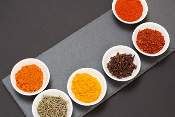 Various ground spices and herbs on stone cutting board.