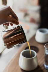 Pouring black coffee from a steel coffee pot into a white porcelain cup, selected focus