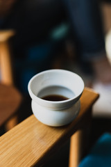 White cup of black coffee on a wooden arm of a chair at the coffee shop