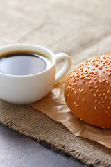 Sesame bun and coffee mug on paper wrapping kraft and on burlap tablecloth.