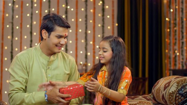 Indian brother gifting her cute little sister her rakhi gift -  Raksha Bandhan concept. Brother gifts her sister a rakhi gift in the acceptance of her sisterly love - Indian customs and rituals