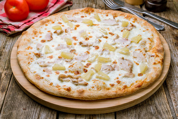 pizza Hawaiian with pineapple and chicken on wooden table