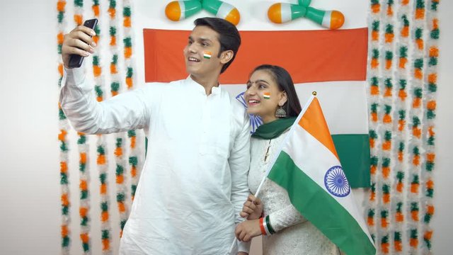 Young Indian teenagers clicking selfie together on Republic Day - National flag background. Young Indian siblings rejoicing freedom day with a selfie with a national flag - patriotic. Independence Day