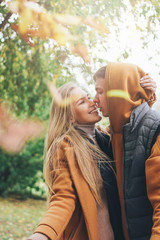 Happy young couple in love teenagers friends dressed in casual style walking together and throws leaves at camera, autumn city street